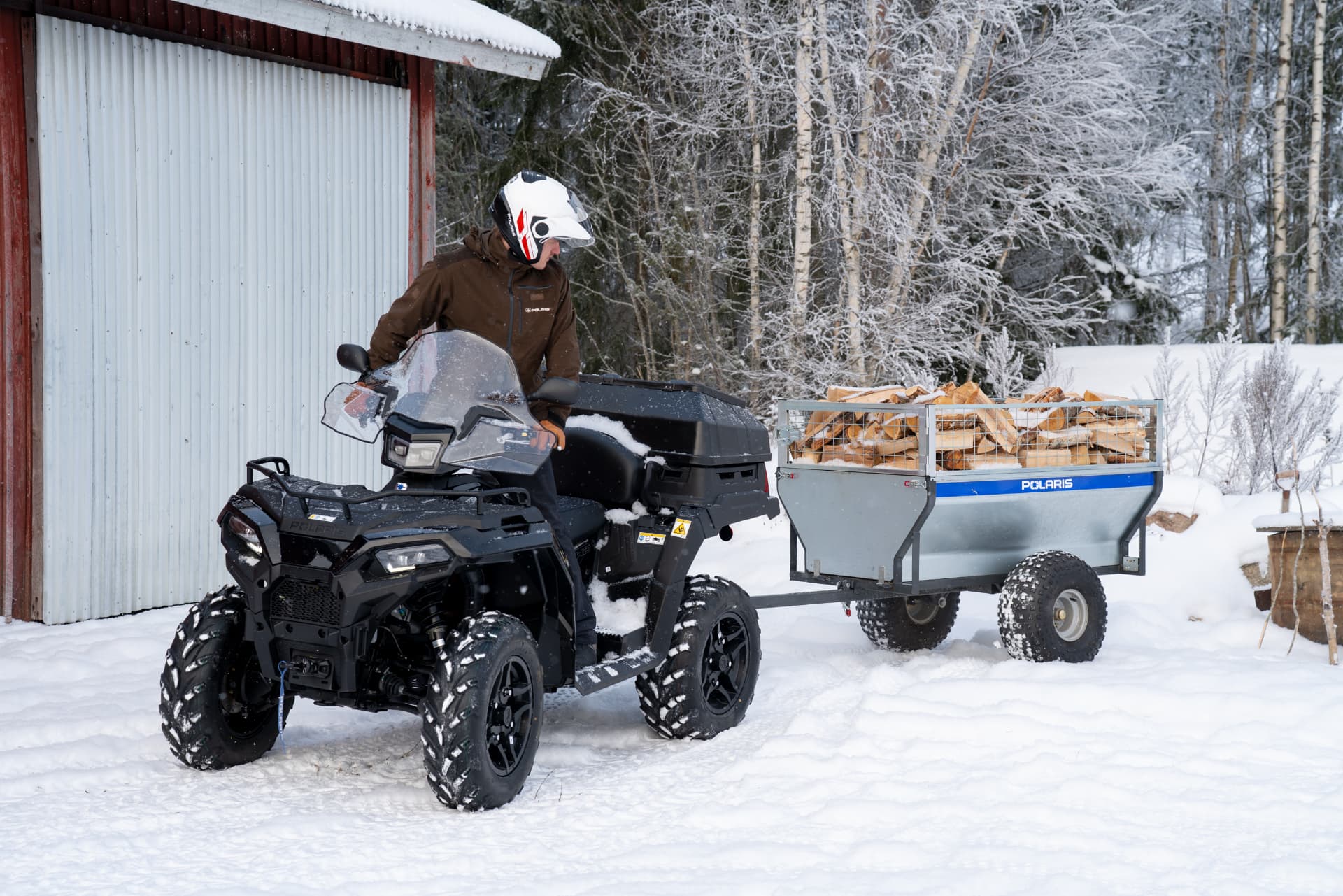Polaris fyrhjuling med skogsvagn i vintermiljö